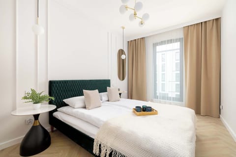A plush emerald green velvet headboard anchors the comfortable double bed, complemented by soft beige curtains and a minimalist black bedside table.