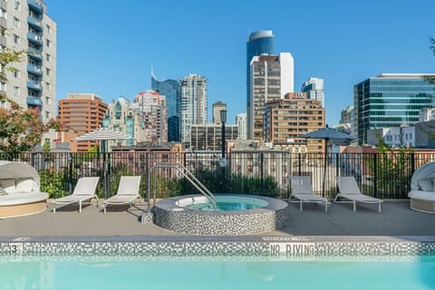 Set against a striking city skyline, the rooftop pool area features a relaxing hot tub and lounge chairs, inviting guests to unwind in a vibrant atmosphere.