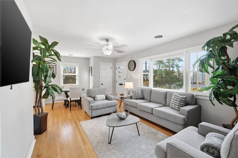 Bright, inviting living room with a large flat-screen TV, comfortable sofa, and two accent chairs—perfect for relaxing after a day out. The oversized window brings in natural light, and the open layout flows into the dining area for easy gathering.