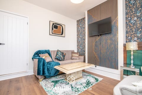 A neutral sofa with a teal throw faces a marble coffee table and a marbled green rug. A wood-slat feature wall with a mounted TV adds a modern, textured focal point to the room.