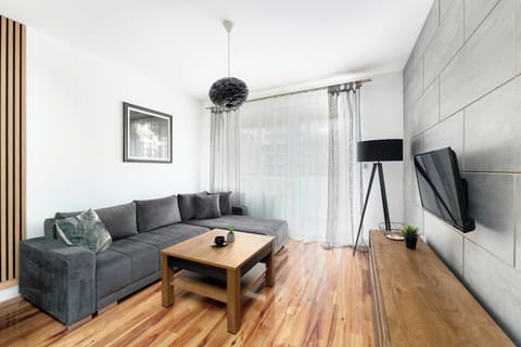 This view of the living room shows a large grey sectional sofa positioned perfectly for watching the wall-mounted flat-screen TV. Large glass doors lead out to a private balcony, flooding the room with light.