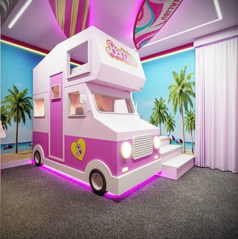 Experience a whimsical playroom with a vibrant pink ice cream truck as a cozy kids' sleeping nook. Enjoy bold tropical wall art and playful lighting, creating a cheerful atmosphere ideal for family fun and adventure.