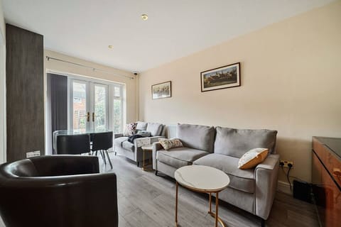 Sitting room with a large grey sofa, leather tub chair, round marble-top side table, and French doors fitted with full-length curtains.