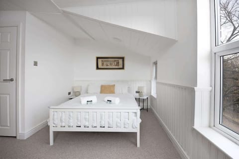 Serene bedroom with crisp white walls, a comfy double bed, and a cozy lounge chair for reading or relaxing. Enjoy your favorite shows on the TV, and let natural light fill the space through the window, creating a peaceful retreat after a busy day.