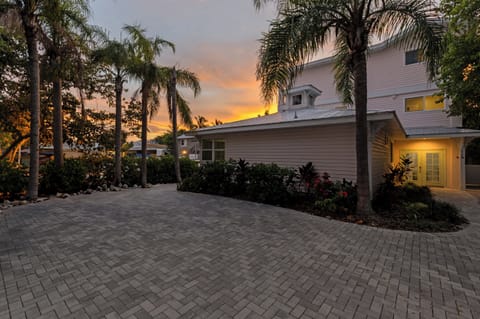 Tropical paradise property surrounded by swaying palms and lush landscaping, with a dramatic sunset painting the sky in golden hues.
