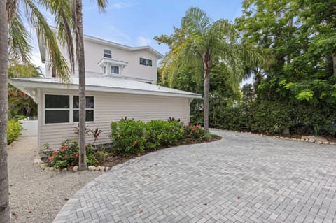 Charming two-story vacation home featuring tropical landscaping with palm trees, lush gardens, and paved parking area.