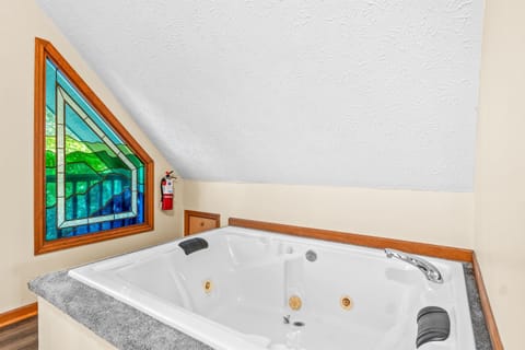 Jetted soaking tub tucked under vaulted ceilings with a stained-glass window for soft natural light. A quiet spot to unwind after a long day exploring Pigeon Forge and the Smokies.