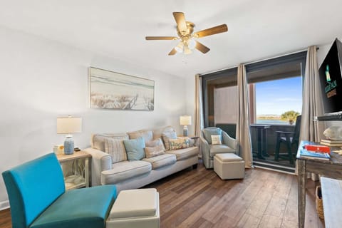 Bright coastal living room with plush seating, smart TV, and sliding glass doors leading to the private balcony.