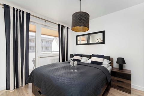 A cozy bedroom features a large double bed with dark bedding and a decorative wooden wall panel. A modern black pendant light hangs from the ceiling, complementing the elegant interior.