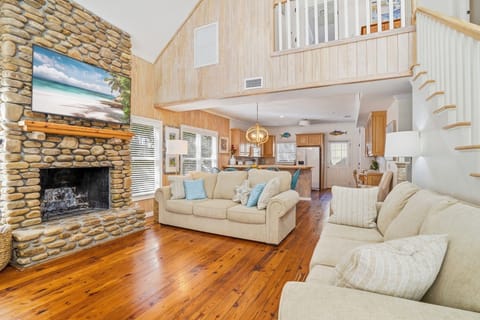 Open Living Room with Stone Fireplace and Loft - Step inside from the covered porch to an open living space with hardwood floors, a floor-to-ceiling stone fireplace, and lofted ceilings above. The layout flows directly into the kitchen and dining area.