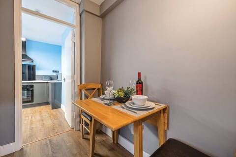 A wooden dining table laid for two with wine glasses, plates, and a wine bottle, with the kitchen visible through the open doorway beyond.