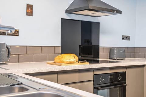 The kitchen worktop shows an induction hob, built-in oven, overhead extractor, microwave, and toaster, with grey subway tiles as a splashback.