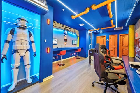 Enjoy our lively game room with striking blue walls and modern lighting. Unwind with friends at the stylish bar seating beside an eye-catching Stormtrooper display, ideal for gaming or relaxing together.