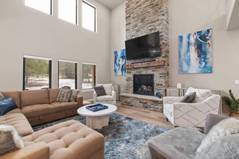 Gather around the stone fireplace in a spacious living room framed by floor-to-ceiling windows, where snowy forest views create the perfect backdrop for relaxation.