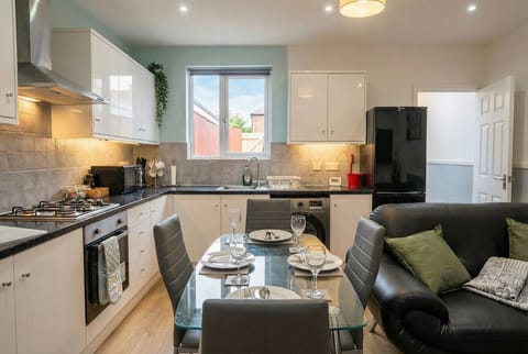 Bright open plan kitchen with gas hob, oven, washing machine, and a table set for four.