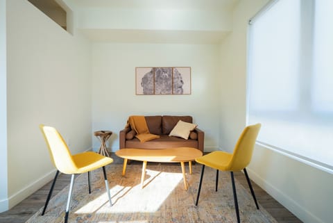 Settle into your stylish living space with warm yellow chairs and a cozy brown sofa, bathed in natural light.