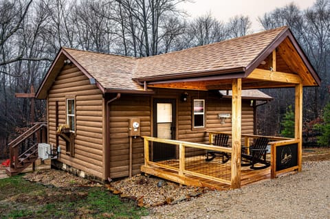 Covered front porch with two black rocking chairs and a wood railing overlooking the gravel driveway.