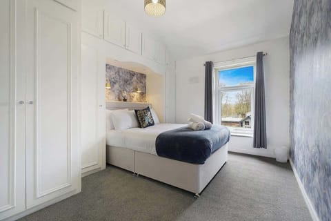 A bright double bedroom offering a comfortable bed dressed in fresh linen, designed for restful sleep. Features include a wall-mounted mirror and two bedside lamps above the headboard, creating a warm and relaxing atmosphere.