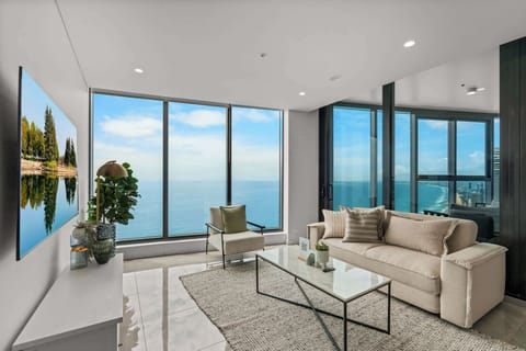 Bright open-plan lounge with queen sofa bed, marble coffee table, smart TV, and panoramic Surfers Paradise beachfront scenery.