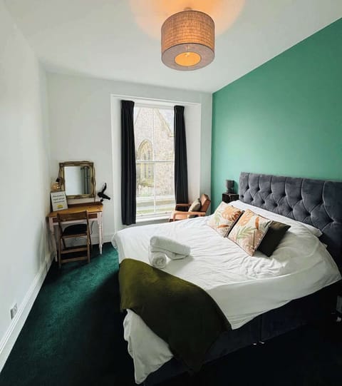 Unwind in this cozy bedroom, featuring a bright window, and a charming table and chair with a mirror, perfect for getting ready or enjoying a quiet moment.