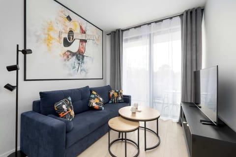The seating area in the living room includes a comfortable blue couch and two round nesting coffee tables. A large window with light grey curtains provides a view of the outside while keeping the interior airy.