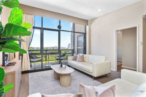 A bright, open-plan living and dining area featuring a modern kitchen with a stone waterfall island and floor-to-ceiling windows that lead to a private balcony with scenic views.
