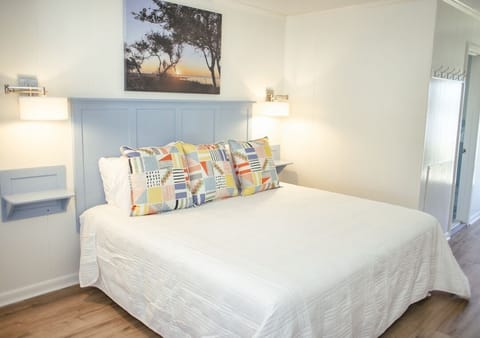 Bright coastal bedroom with plush bed, sconces, and wood floors