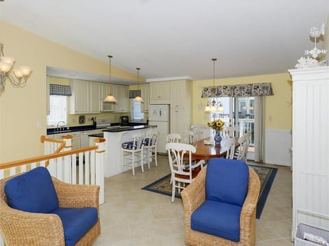 This inviting kitchen, dining, and living areas blend seamlessly, exhibiting modern coastal design with soft yellow walls and comfortable seating options.