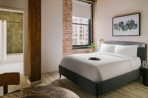 Spacious queen bed studio with exposed brick, large windows, 50 inch smart TV, and hotel quality linens