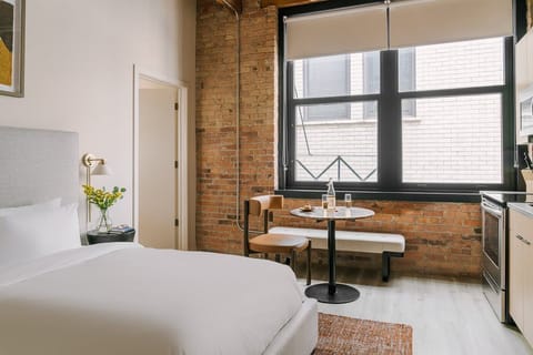 Bright queen bedroom with exposed brick, large windows, and hotel quality linens