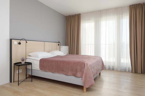 Bright studio space with a comfortable double bed positioned near large windows, creating an airy and welcoming atmosphere.