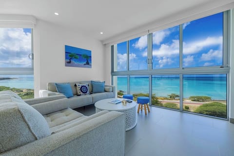 Your bright living space frames stunning turquoise waters through floor-to-ceiling windows, where you can relax on plush seating while soaking in endless ocean views.