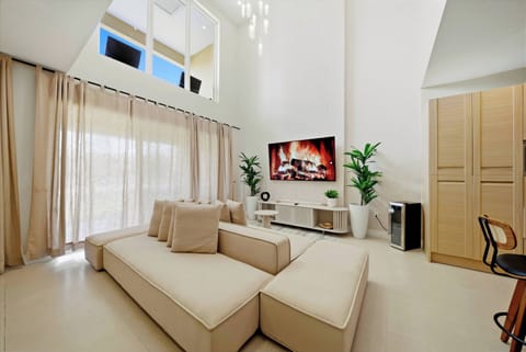 Unwind in the spacious living area with a stylish sectional sofa and tall windows that bathe the space in natural light. The modern decor and lush greenery create an inviting atmosphere perfect for relaxing after your adventures.