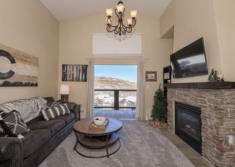 Unwind in your cozy living room with stone fireplace, elegant chandelier, and mountain views through sliding doors to your private balcony.