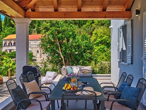 Savor outdoor dining on this shaded terrace with exposed wooden beams. A modern table and grill overlook lush greenery.