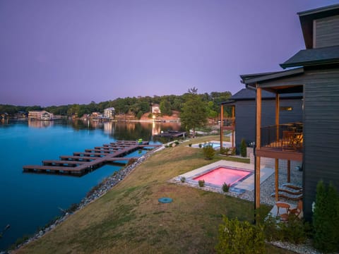 Breathtaking dusk view showcasing the private illuminated pool, sprawling sloping lawn, and quiet lakefront surroundings.