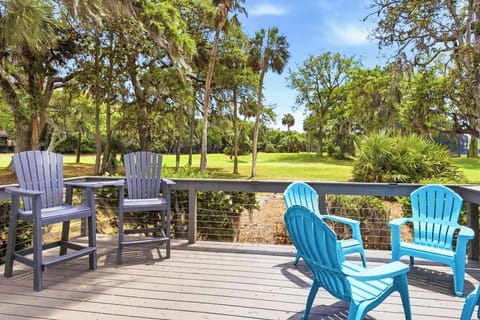 Colorful Adirondack chairs on the back deck overlook a lush lawn framed by majestic live oaks draped in Spanish moss.