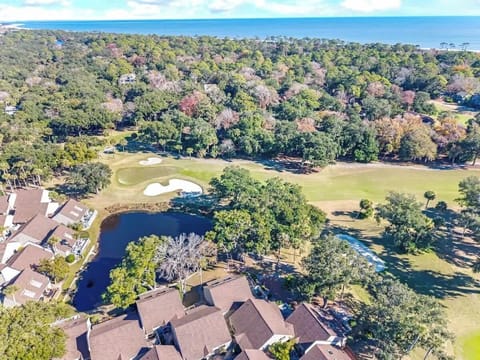 Aerial view showcasing the property's prime location overlooking championship golf greens with ocean views beyond the coastal forest.