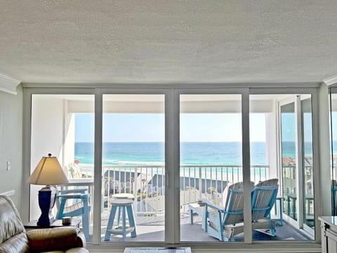 Step into your beachfront haven where floor-to-ceiling windows frame endless ocean views and your private balcony awaits with comfortable seating.