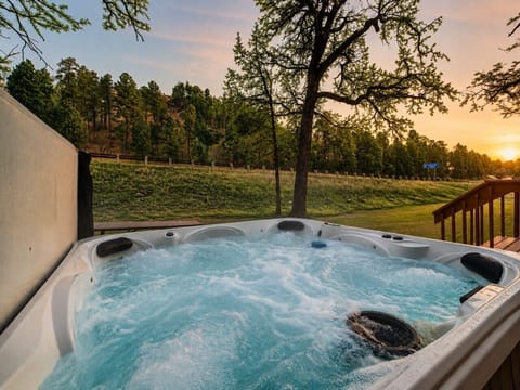 Bubbling hot tub with open Black Hills views, peaceful greenery, and a soft sunset glow.