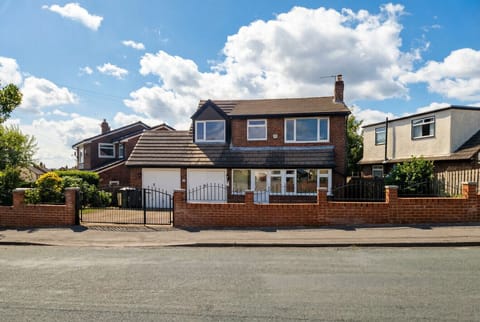 Red-brick detached house with a tiled roof, metal railings, and a front garden photographed under a clear blue sky.