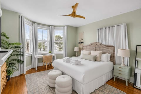 A grand primary retreat with a decorative fireplace, workspace, TV, and sun-filled windows.