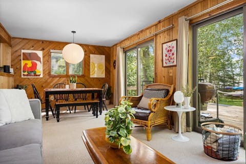 Cozy wood-paneled living and dining space with warm natural light, deck access, and relaxing cottage charm.