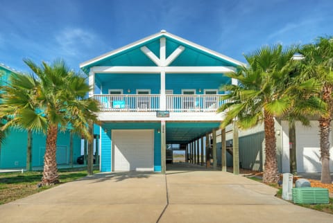Bright coastal stilt home with palm-lined driveway and breezy balcony.