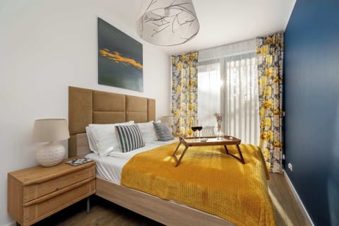 A master bedroom featuring a plush brown headboard and a bed accented with a vibrant yellow throw blanket. A dark blue wall provides a bold contrast to the light neutral tones of the room.