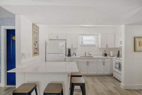 The modern kitchenette showcases sleek white cabinetry, a breakfast bar with stools, and ample natural light, ideal for cooking and gathering.