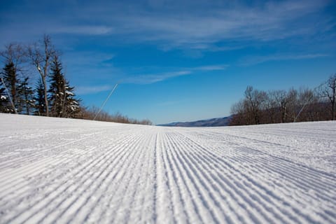 Expansive and well-groomed slopes stretch invitingly into the distance, showcasing the perfect conditions for endless snow sports against the backdrop of tranquil, snowy Vermont terrain.