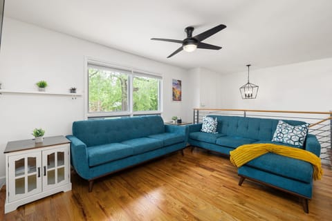 Bright living room with blue sectional, hardwood floors, and leafy window views