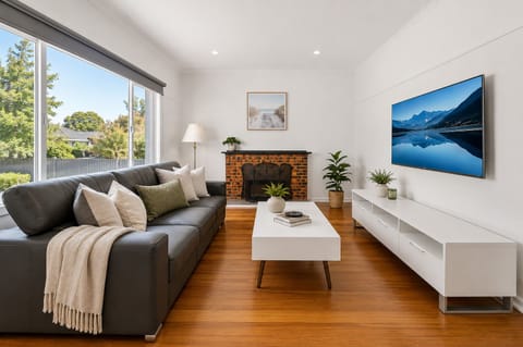 Sunny lounge with leather sofa, smart TV, cozy brick fireplace, hardwood floors