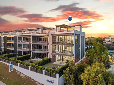 Modern beachfront apartments beneath a spectacular sunset sky, surrounded by lush tropical gardens and contemporary architecture.